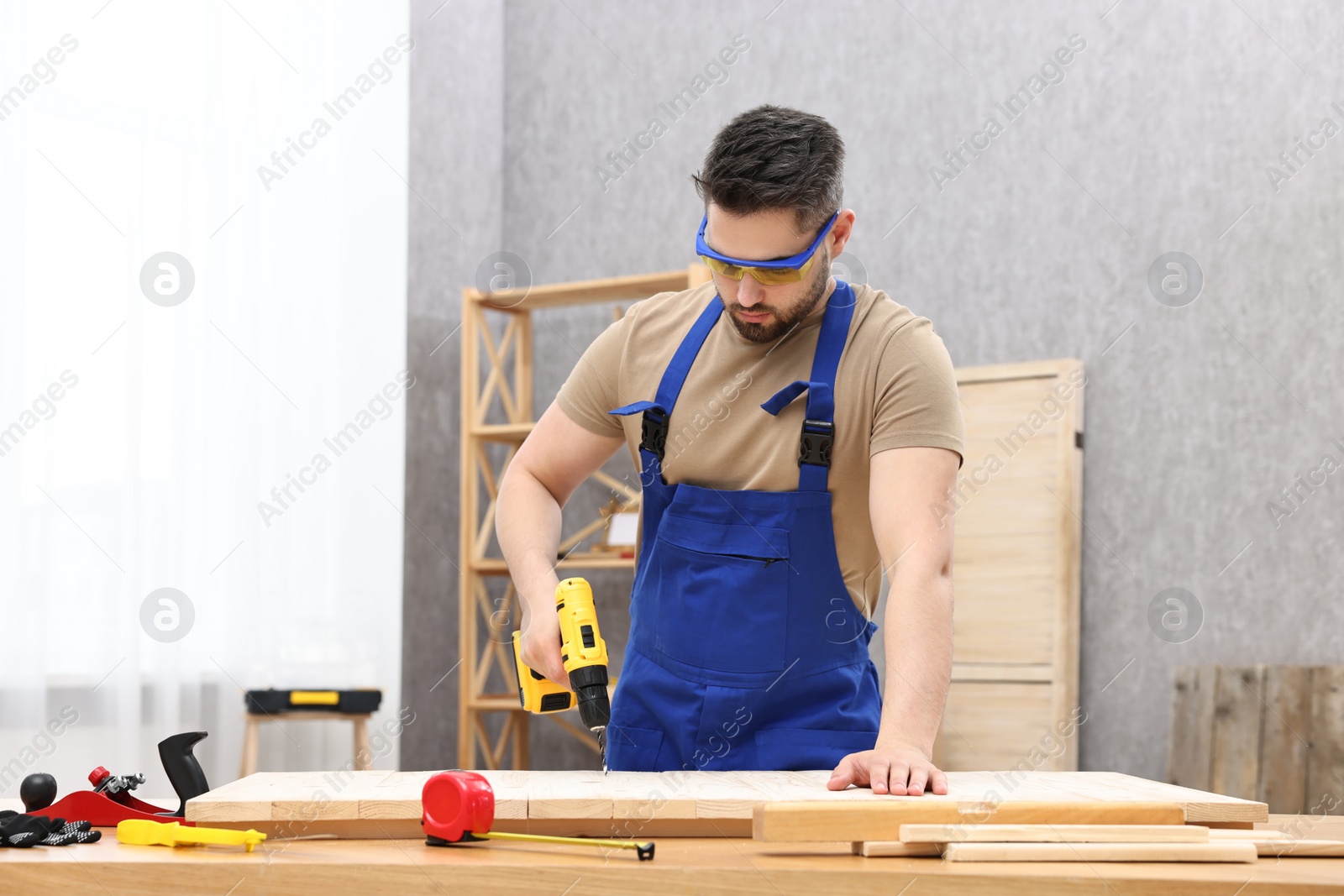 Photo of Young worker using electric drill at table in workshop