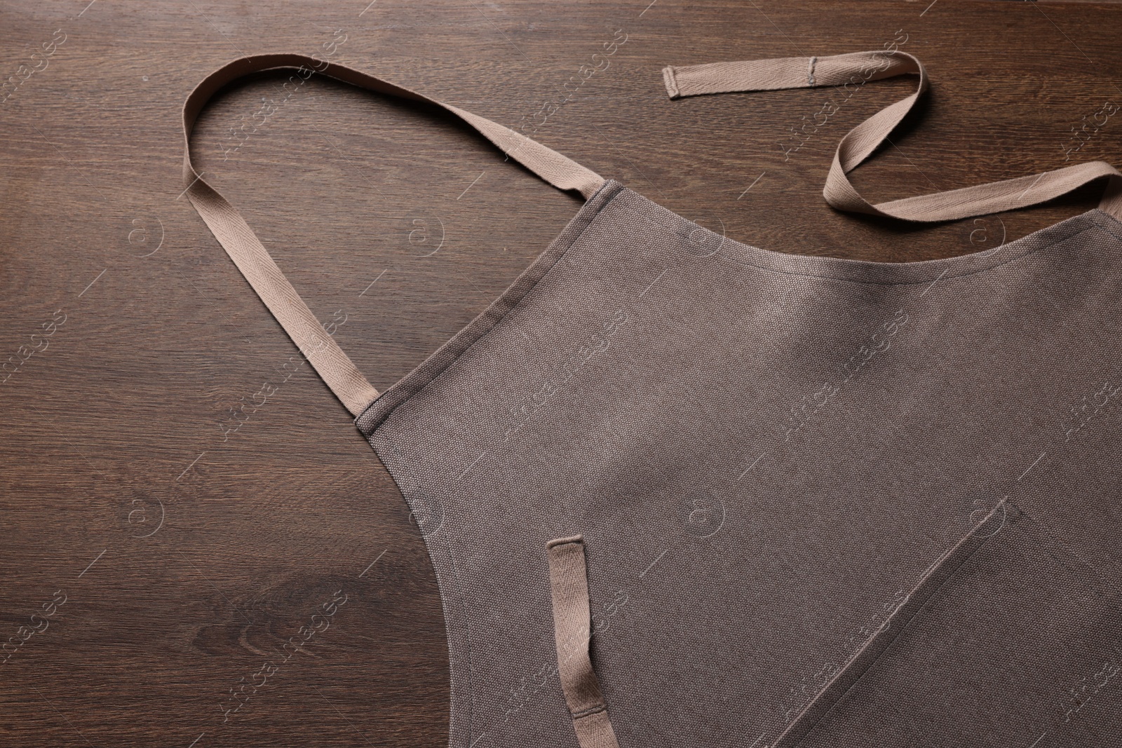 Photo of Stylish brown apron on wooden table, top view. Mockup for design