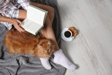 Woman with cute red cat and book on floor, top view. Space for text