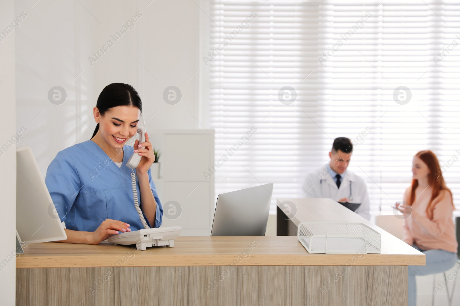 Photo of Receptionist talking on phone while doctor working with patient in hospital