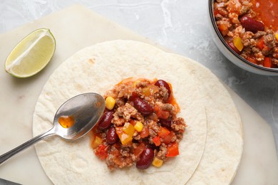 Photo of Tasty chili con carne with tortillas on light table, flat lay