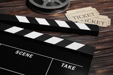 Photo of Clapperboard, movie tickets and film reel on wooden table, closeup