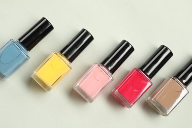 Colorful nail polishes in bottles on light background, flat lay