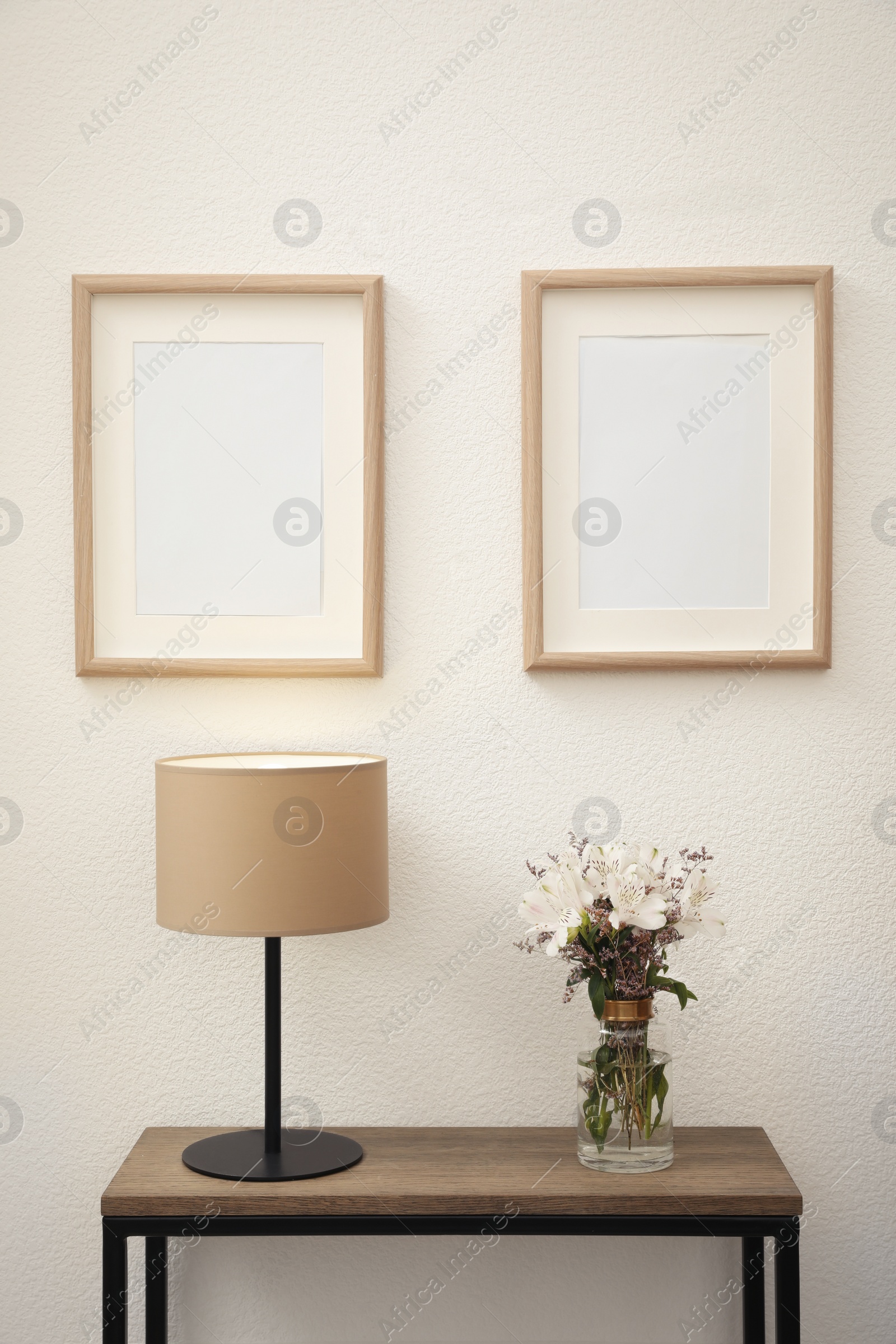 Photo of Bouquet with alstroemeria flowers and lamp on console table near white wall indoors. Interior design