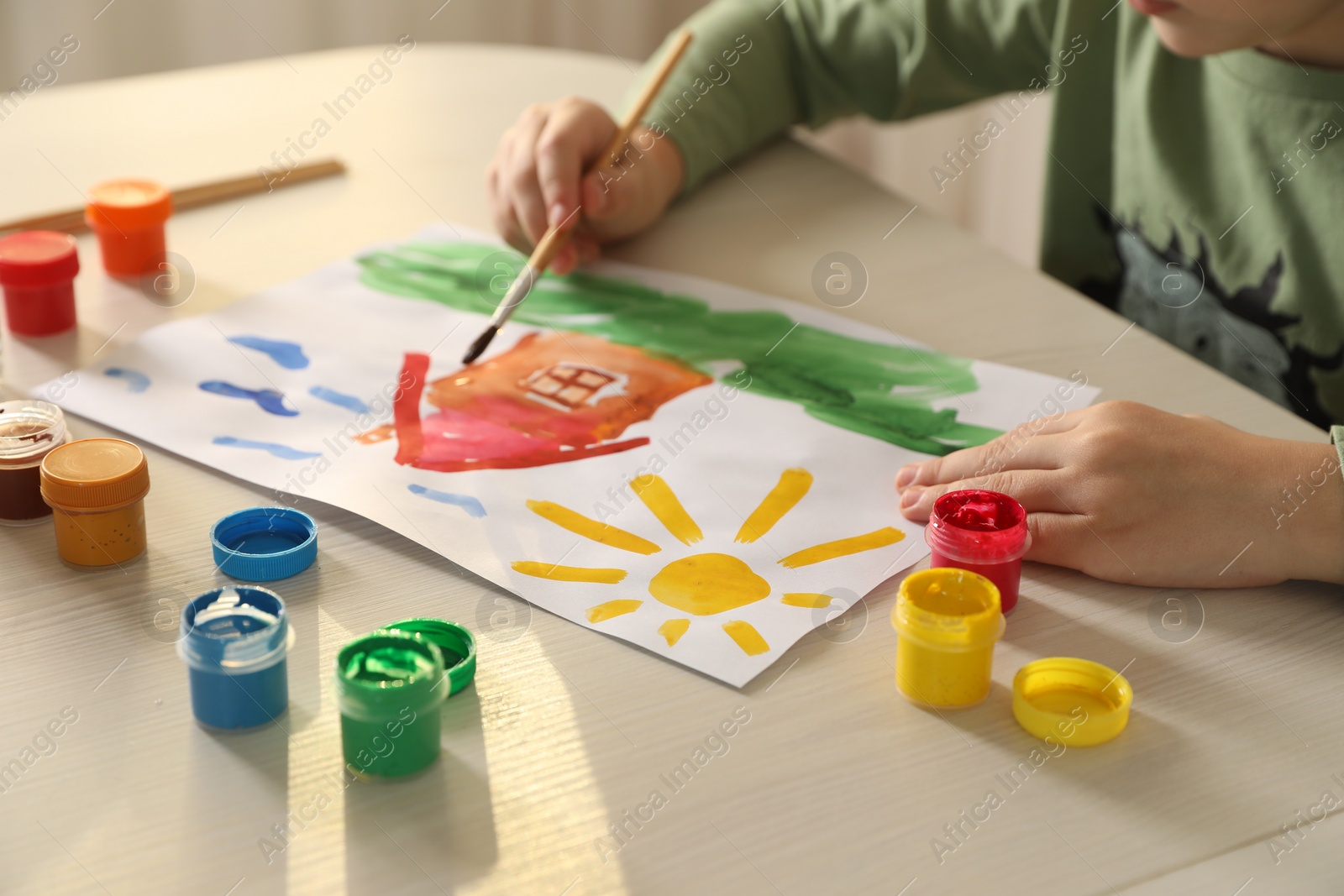 Photo of Little boy drawing picture with brush at wooden table indoors, closeup. Child`s art