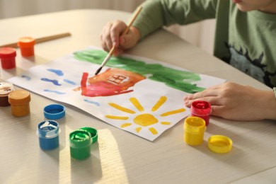 Little boy drawing picture with brush at wooden table indoors, closeup. Child`s art