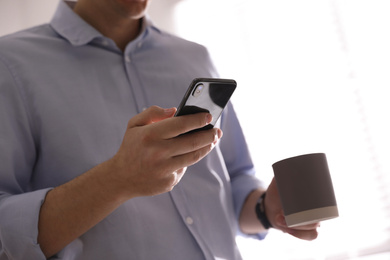 Photo of Man with cup and smartphone against light background, closeup of hands