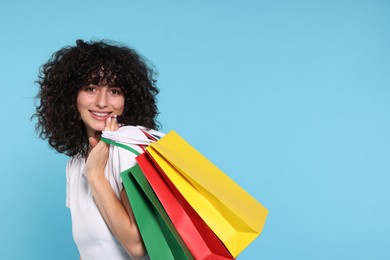 Happy young woman with shopping bags on light blue background. Space for text