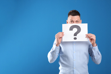 Emotional man holding paper with question mark on blue background. Space for text