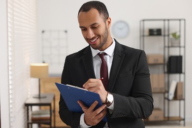 Smiling young man with clipboard writing notes in office. Lawyer, businessman, accountant or manager