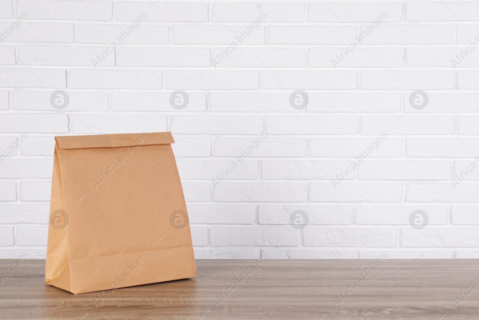 Photo of Paper bag on table against brick wall. Mockup for design