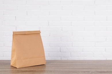 Photo of Paper bag on table against brick wall. Mockup for design