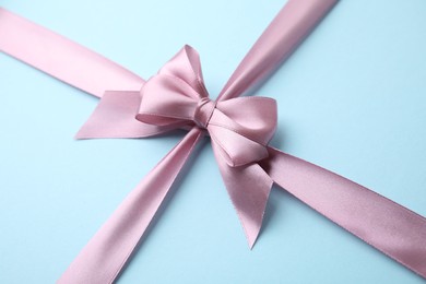 Photo of Pink satin ribbon with bow on light blue background, closeup