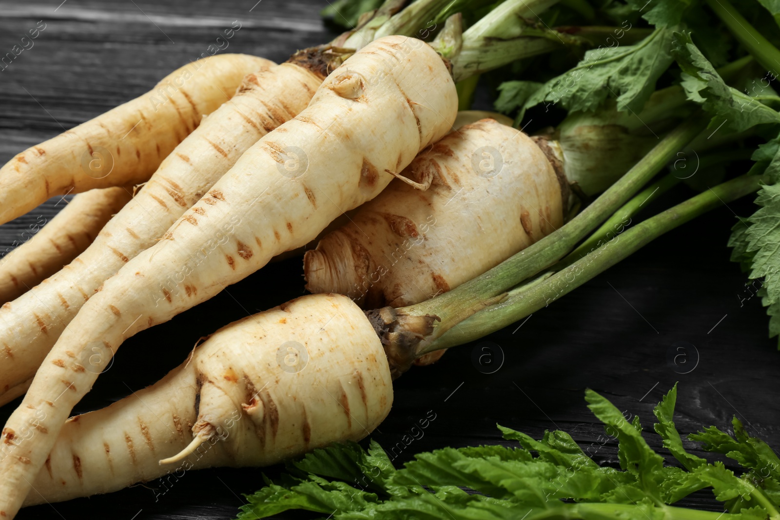 Photo of Tasty fresh ripe parsnips on black wooden table, closeup