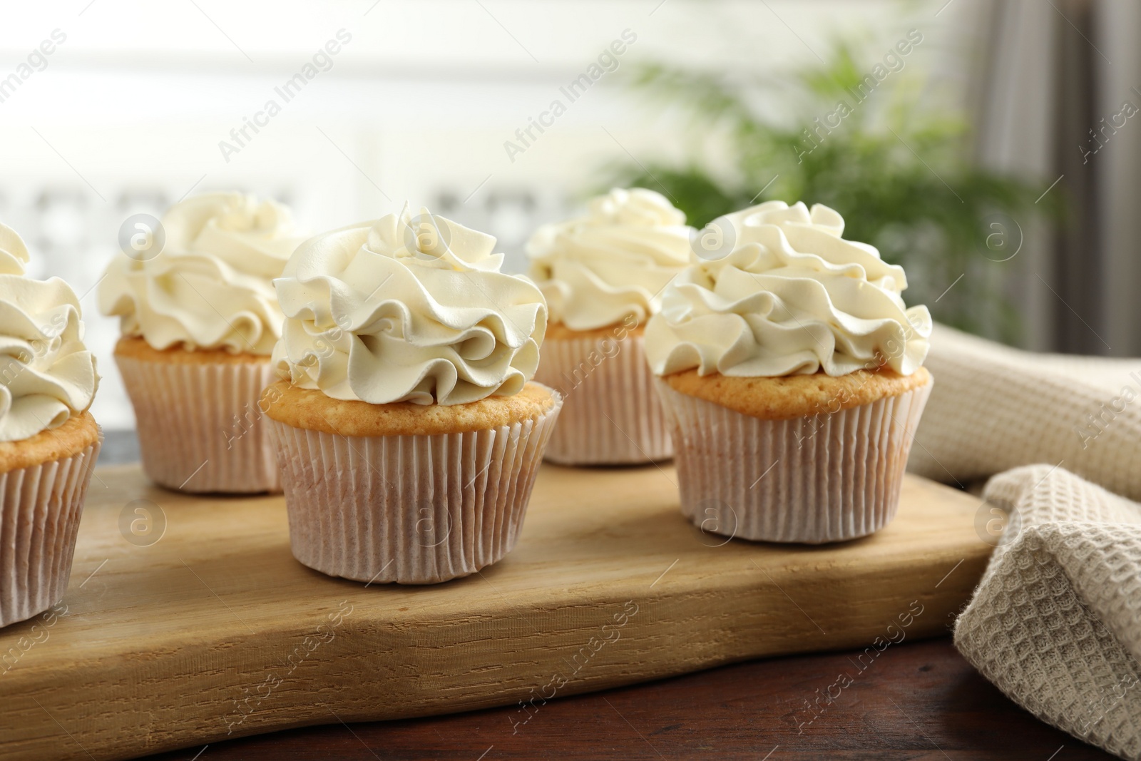 Photo of Tasty cupcakes with vanilla cream on wooden table, closeup