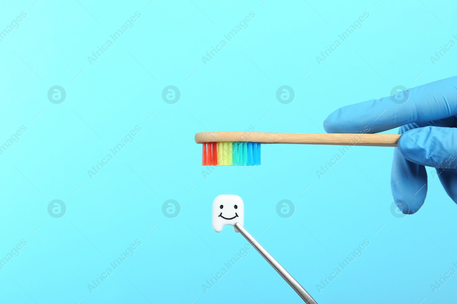 Photo of Dentist holding wooden brush near small plastic tooth on color background. Space for text