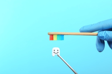 Photo of Dentist holding wooden brush near small plastic tooth on color background. Space for text