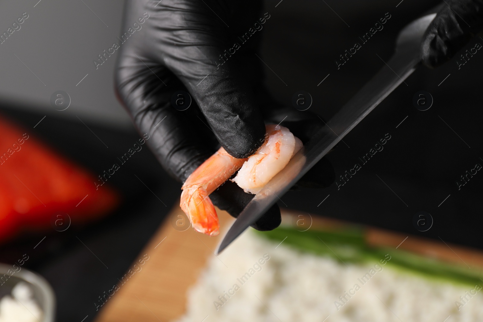 Photo of Chef in gloves peeling shrimp for sushi roll at table, closeup