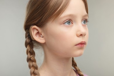 Photo of Little girl with hearing aid on grey background, closeup