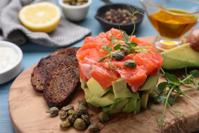 Delicious salmon tartare served with avocado and croutons on light blue table, closeup