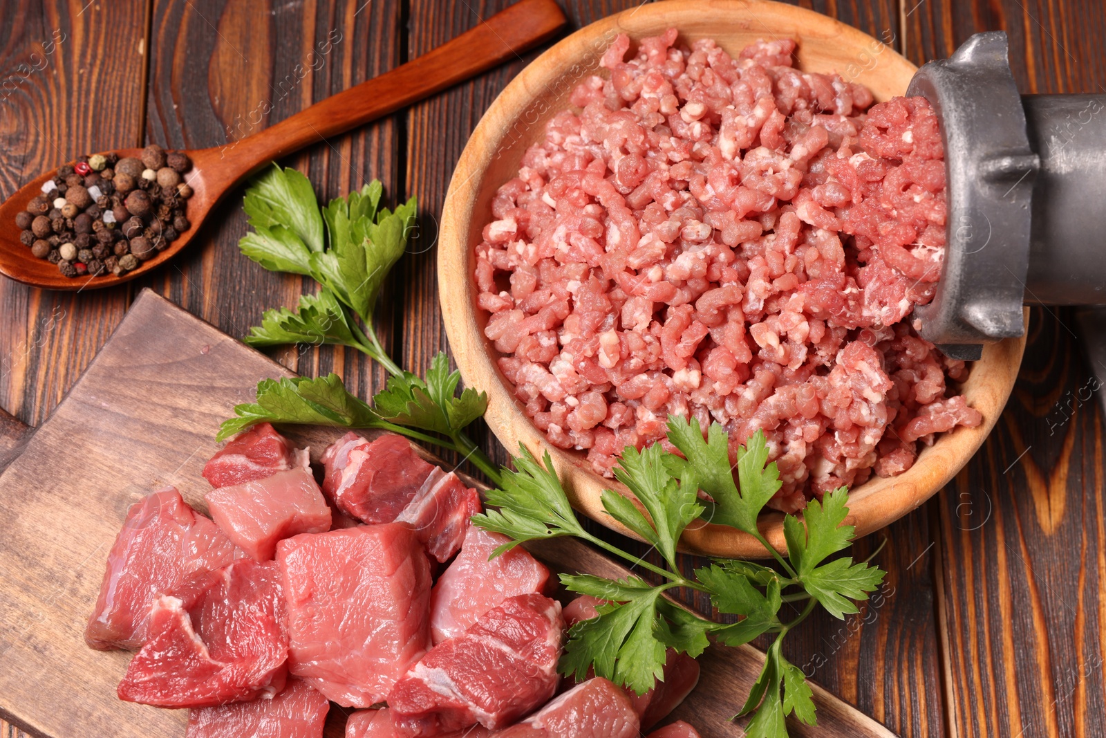 Photo of Manual meat grinder with beef, parsley and peppercorns on wooden table, above view