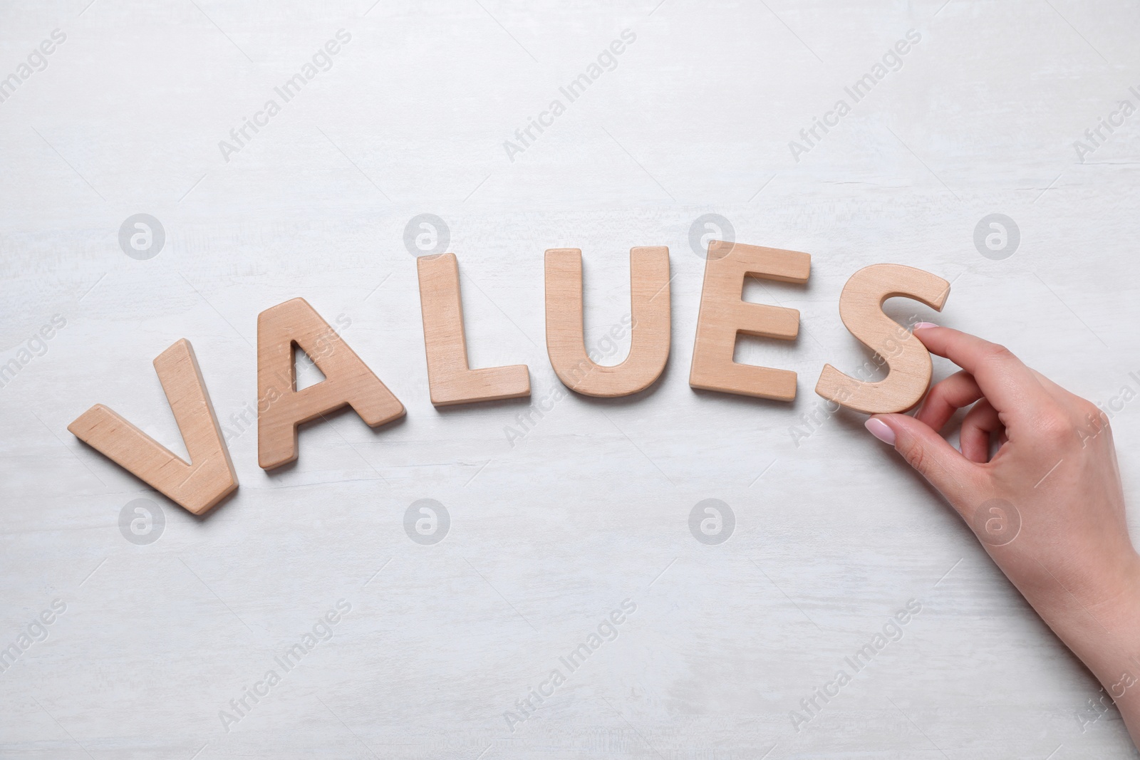 Photo of Woman making word VALUES of wooden letters on white background, top view