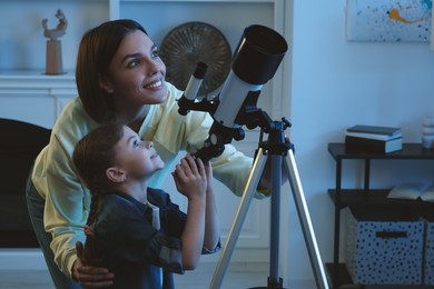 Photo of Happy mother and her cute daughter using telescope to look at stars in room