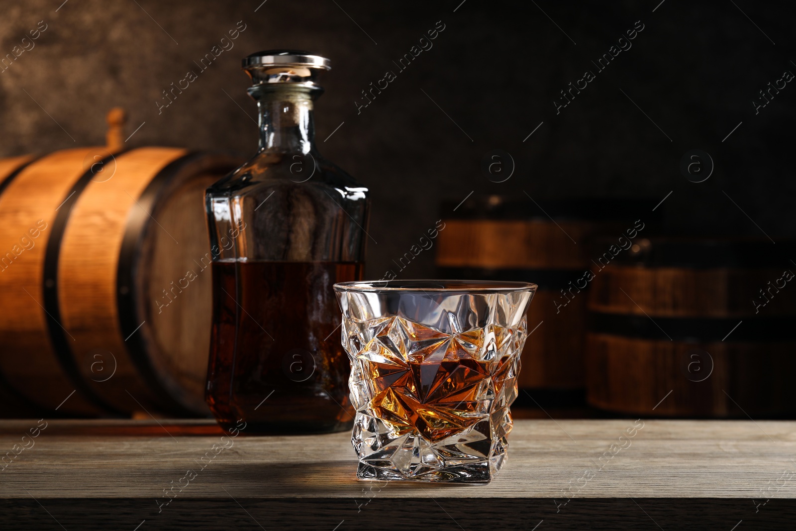 Photo of Glass with whiskey on table against wooden barrels