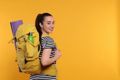 Photo of Smiling young woman with backpack on orange background, space for text. Active tourism