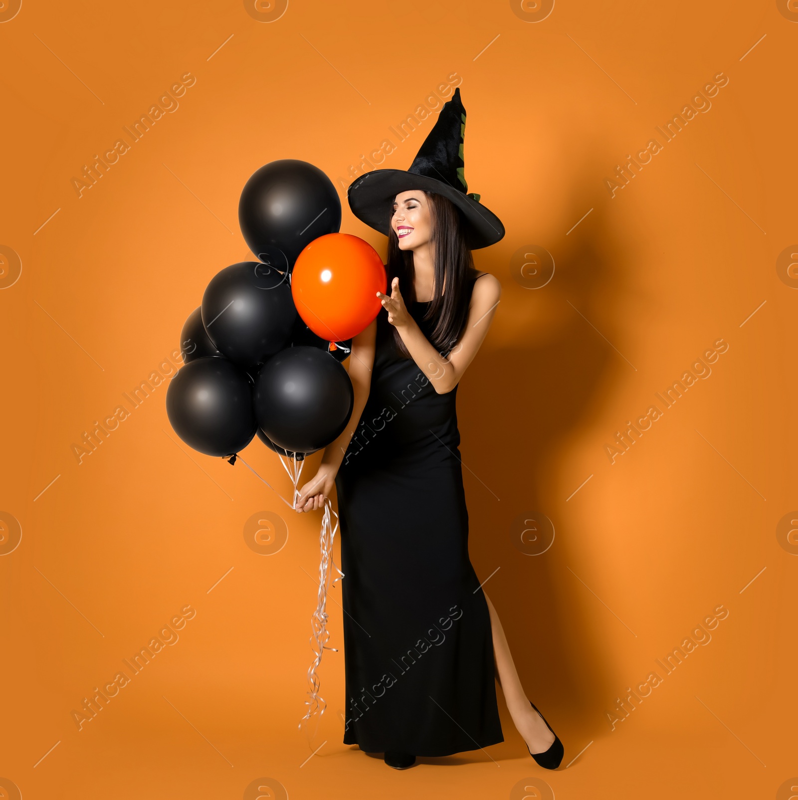 Photo of Beautiful woman wearing witch costume with balloons for Halloween party on yellow background