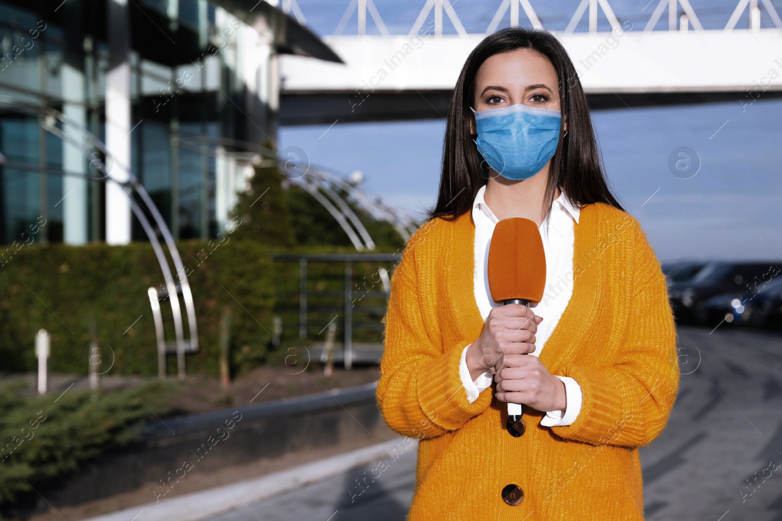 Image of Young journalist with medical mask and microphone working on city street. Virus protection