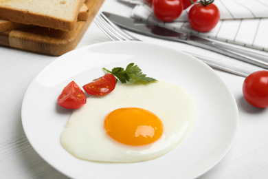 Photo of Tasty fried egg with parsley and tomato on white wooden table, closeup