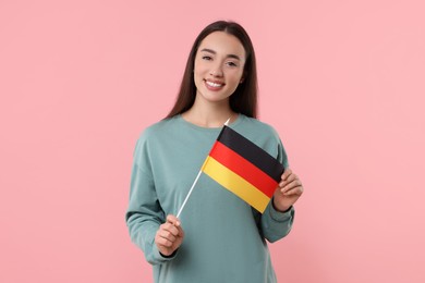 Young woman holding flag of Germany on pink background