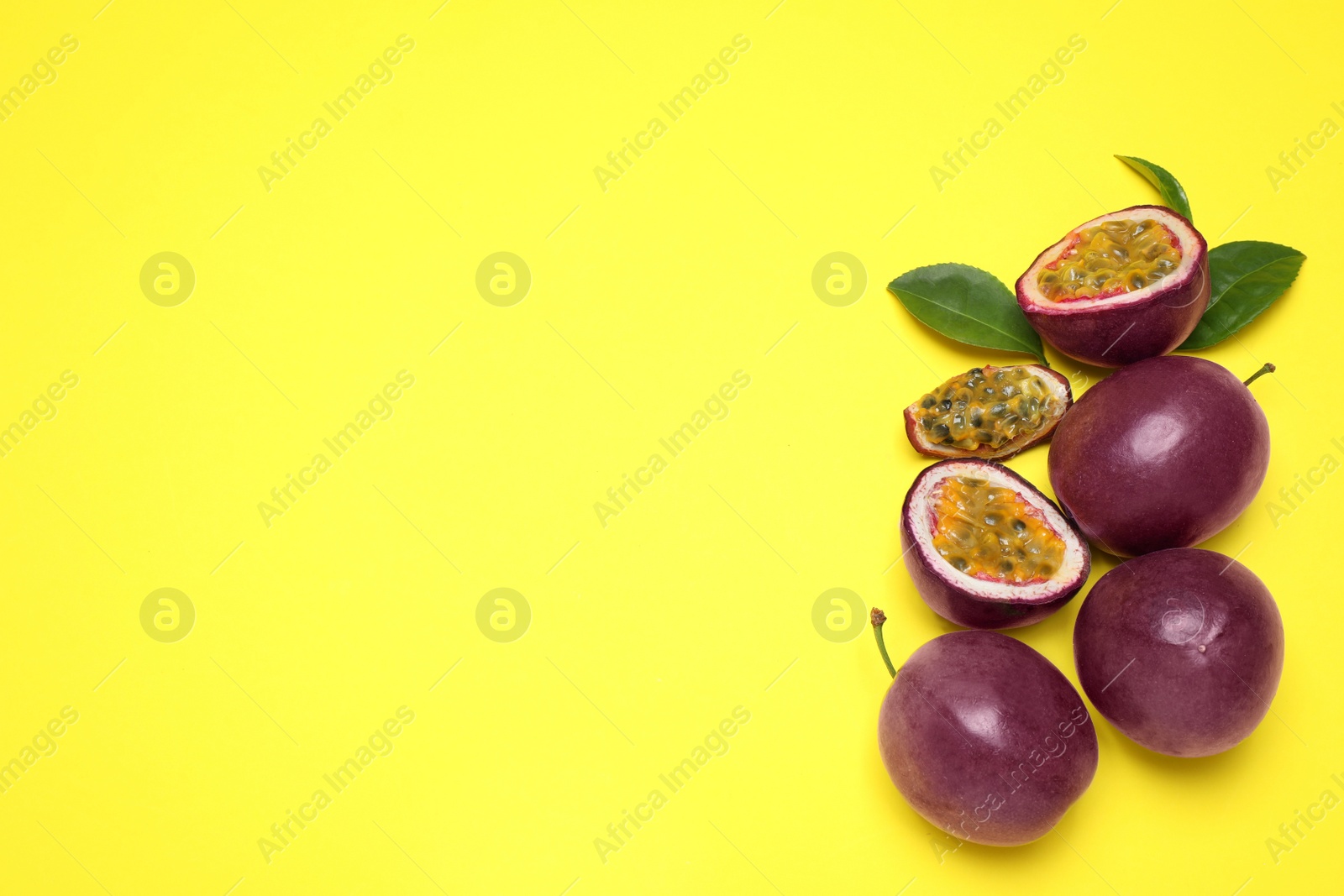 Photo of Fresh ripe passion fruits (maracuyas) with green leaves on yellow background, flat lay. Space for text