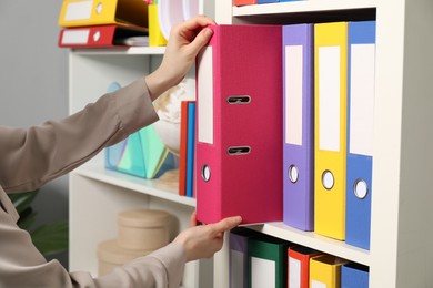 Photo of Woman taking binder office folder from shelving unit indoors, closeup