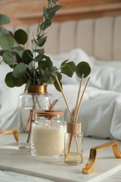 Photo of Eucalyptus branches, candle and aromatic reed air freshener on bed indoors, closeup. Interior elements