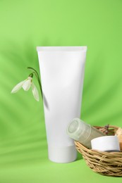 Photo of Cream, shampoo sample, lip balm and snowdrop flower on light green background