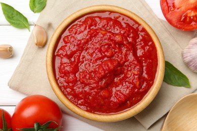Photo of Homemade tomato sauce in bowl and fresh ingredients on white wooden table, flat lay