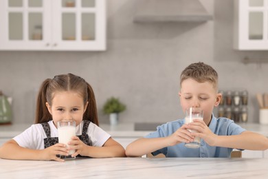 Photo of Cute children drinking fresh milk from glasses at white table in kitchen