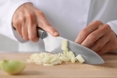 Professional chef cutting onion at wooden table, closeup