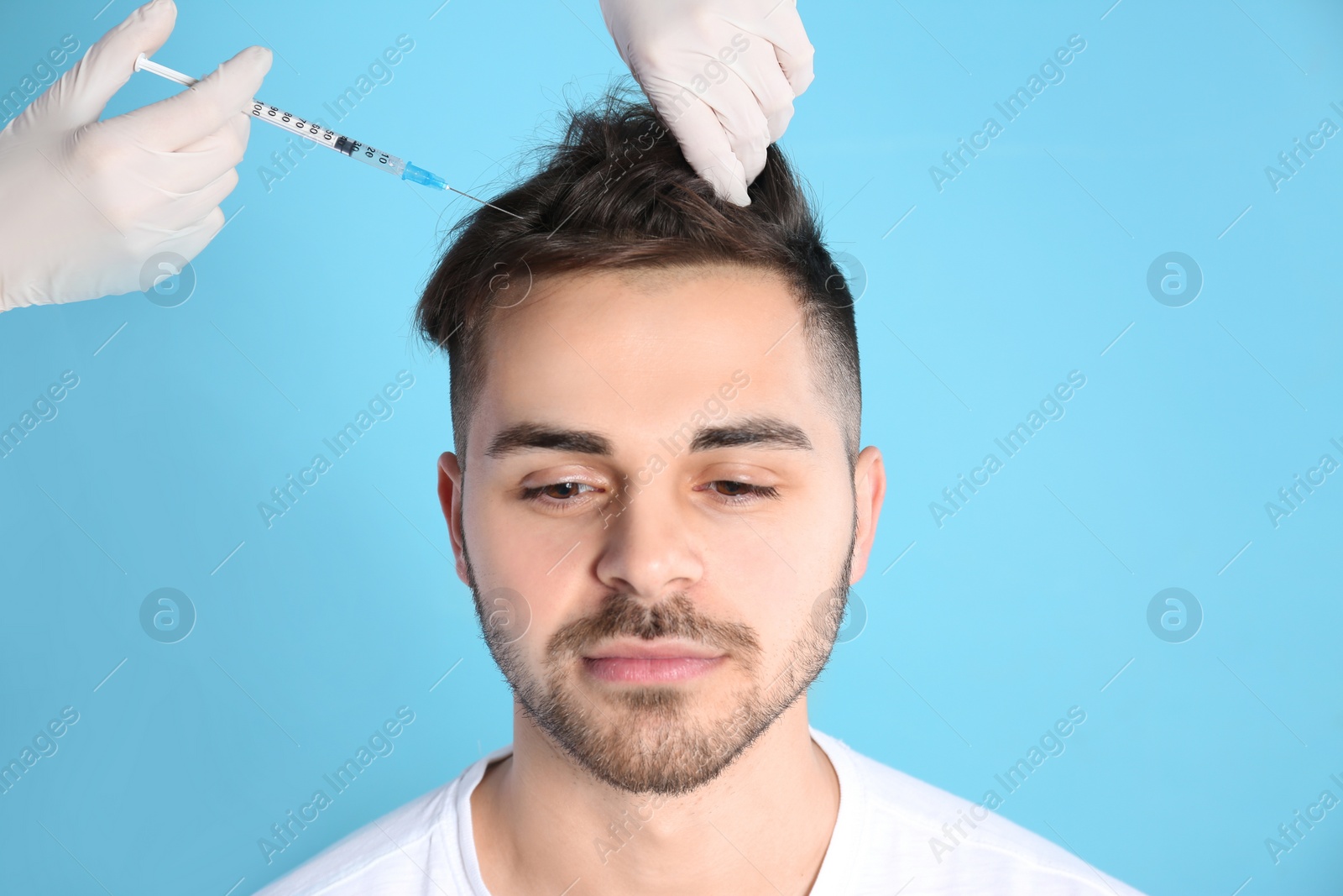 Photo of Young man with hair loss problem receiving injection on color background