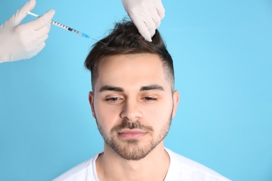 Young man with hair loss problem receiving injection on color background