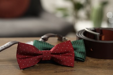 Photo of Stylish color bow ties, wristwatch and belt on wooden table, closeup