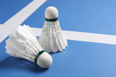 Feather badminton shuttlecocks on blue background, closeup. Space for text