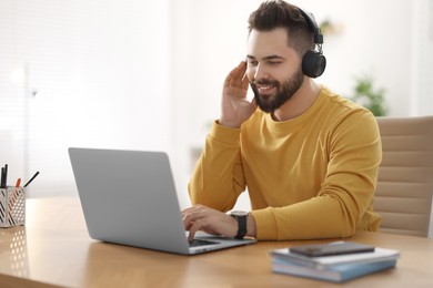 Photo of Young man in headphones watching webinar at table in room