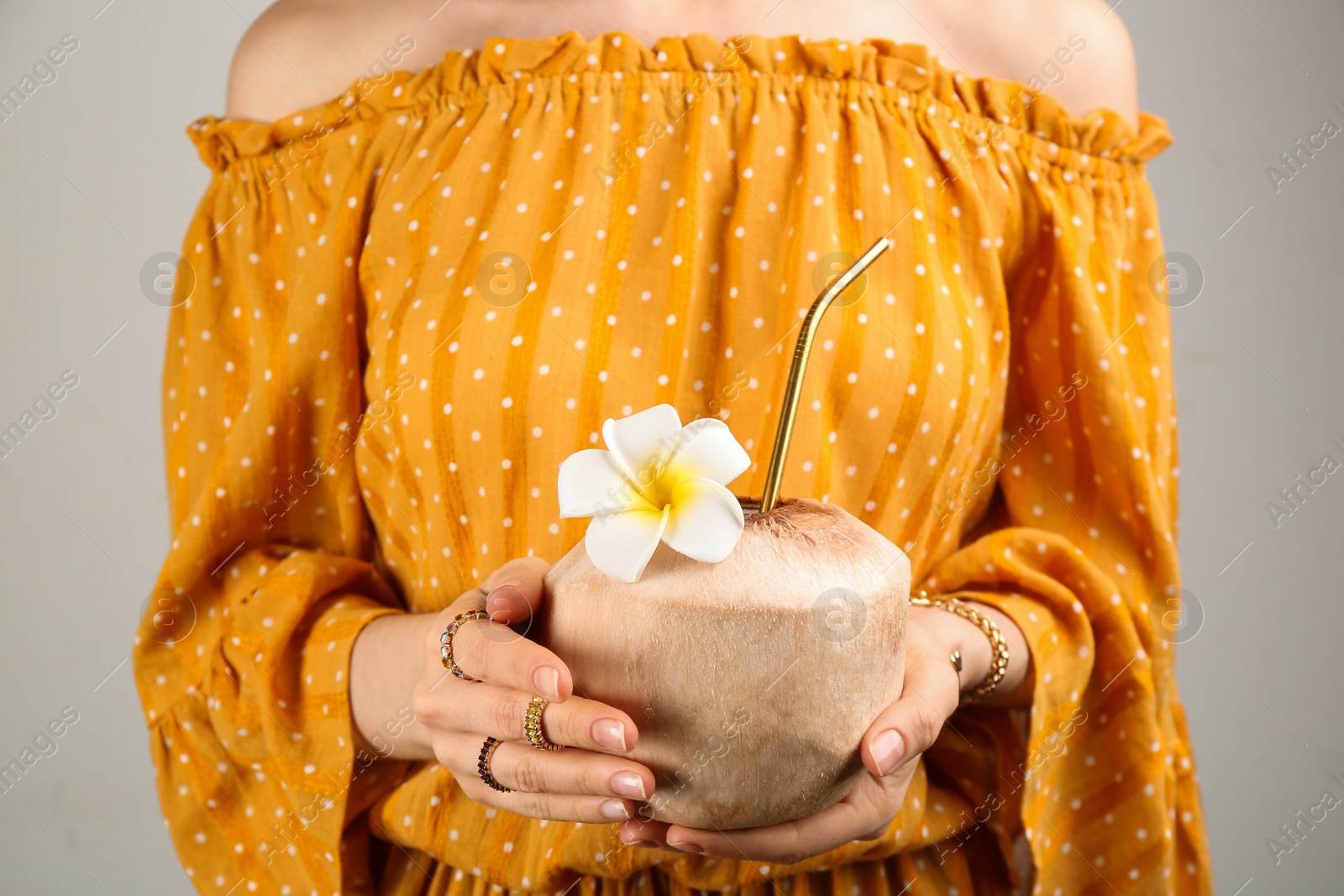 Photo of Woman holding fresh young coconut with straw on grey background, closeup