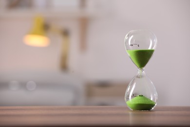 Hourglass with light green flowing sand on table against blurred background. Space for text