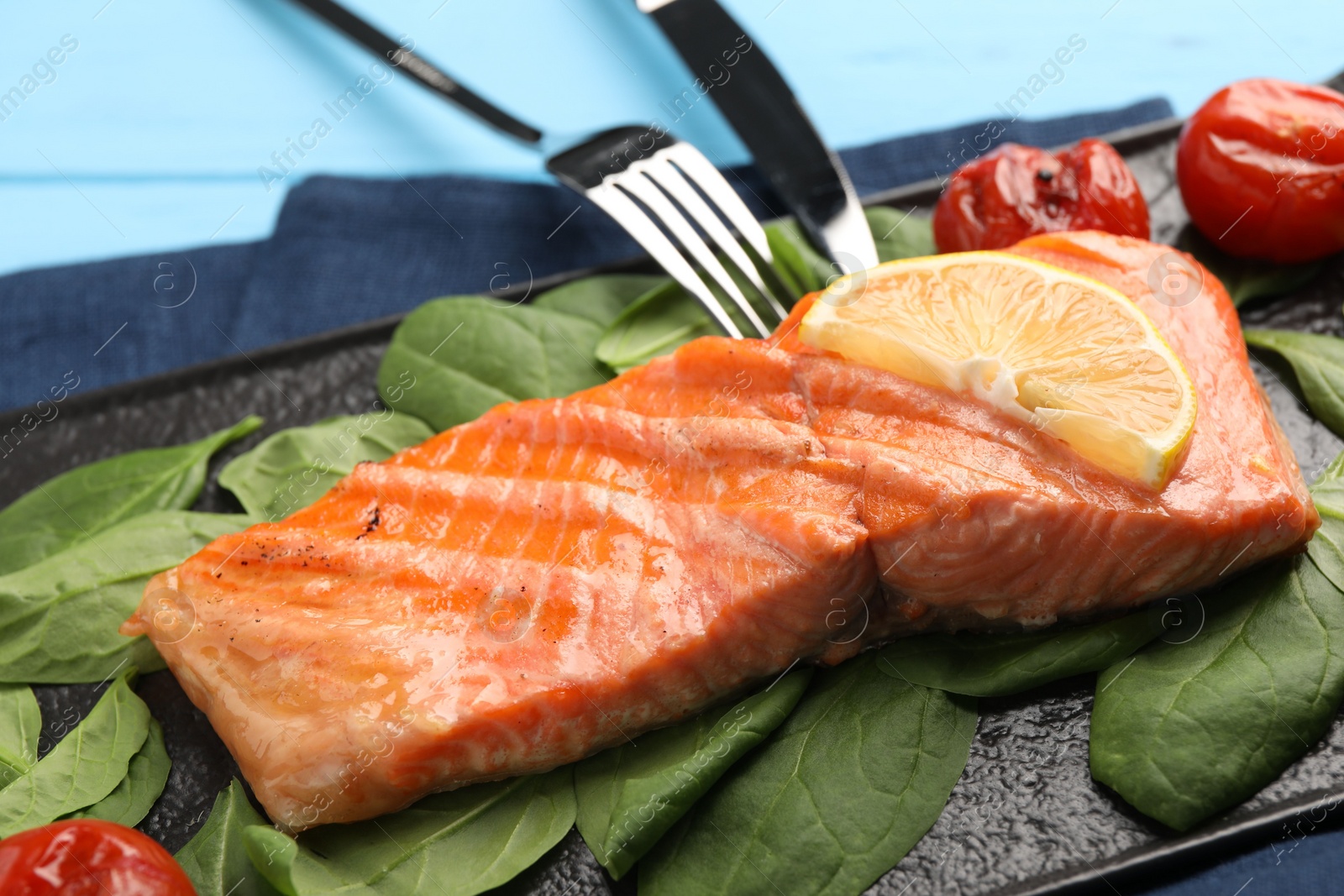 Photo of Tasty grilled salmon with tomatoes, spinach and lemon served on table, closeup