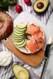 Photo of Delicious bagel with cream cheese, salmon and avocado on table, flat lay