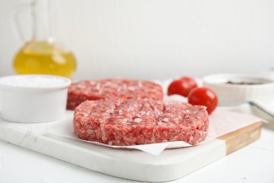 Photo of Raw hamburger patty with salt on white table, closeup